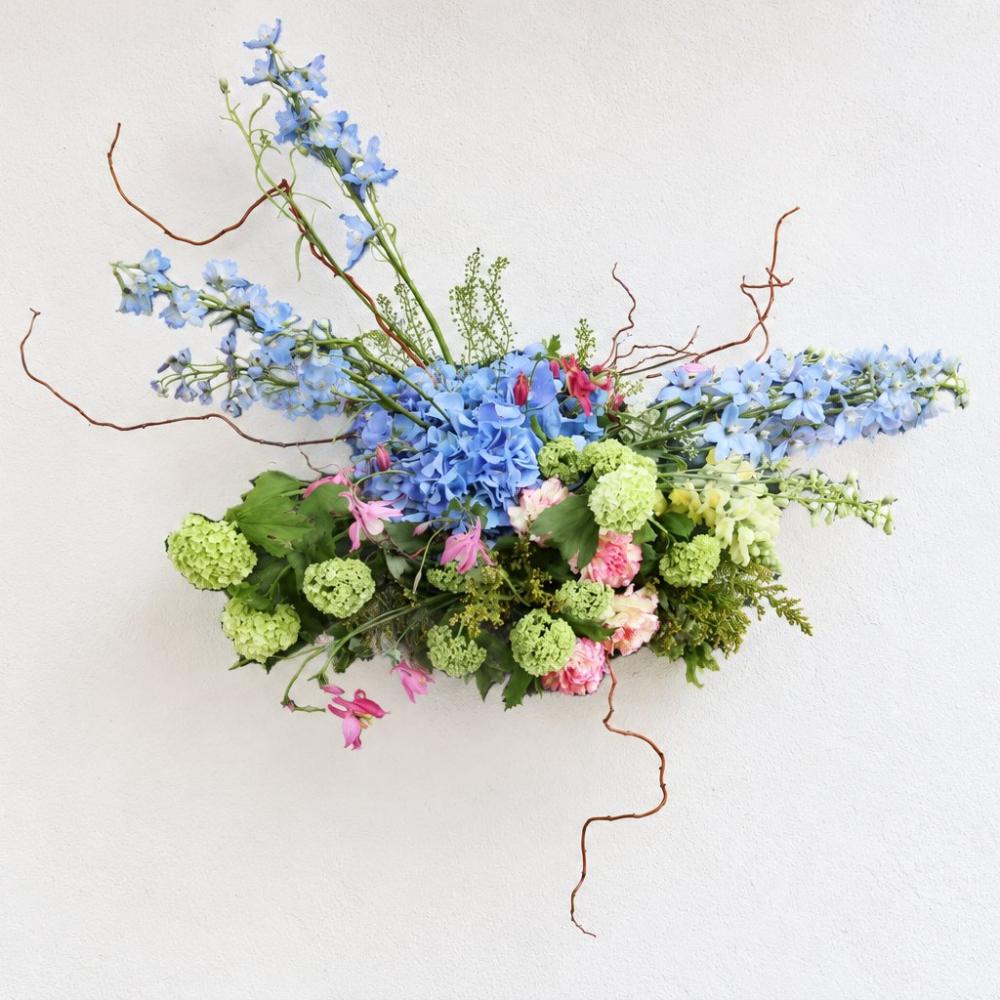 Hanging arrangement with blue delphinium, hydrangea, and pink accent flowers with curly willow branches