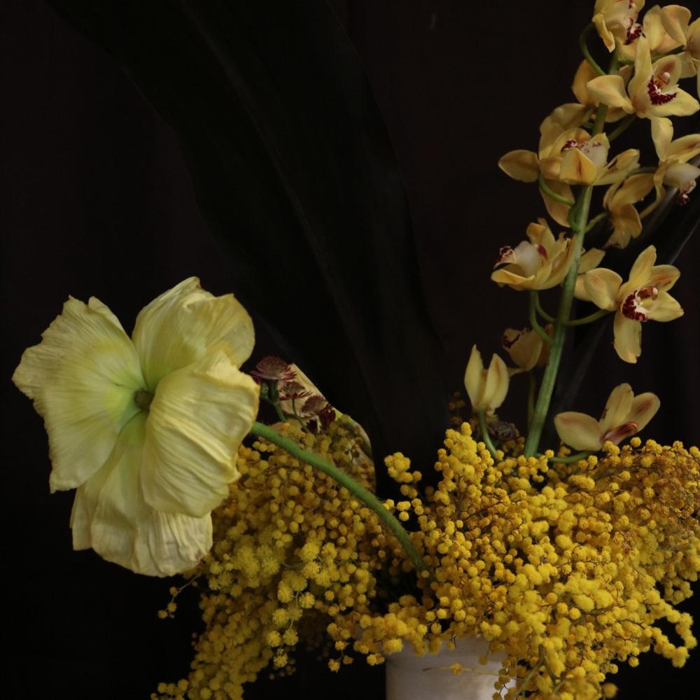Close-up of a pale yellow poppy bloom among orchids and mimosa at Royal Highness, Fitzroy, Berlin