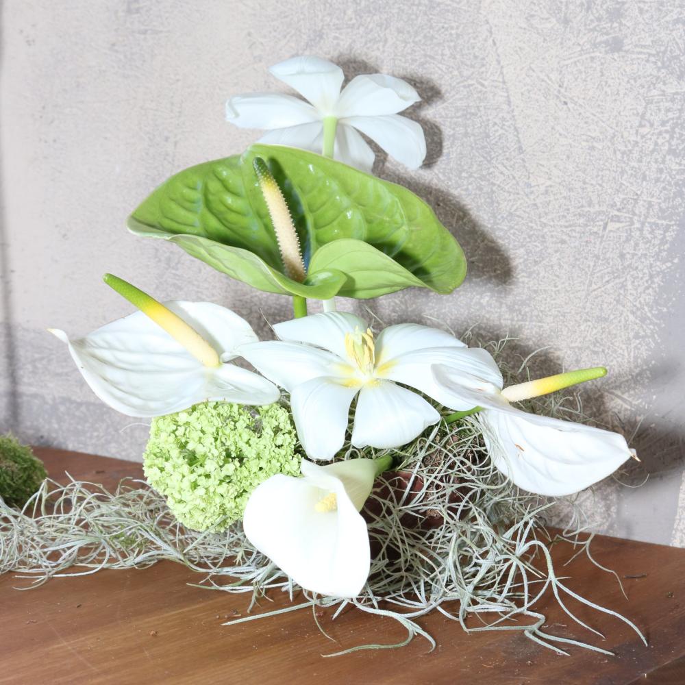 Styled floral arrangement with green anthurium, white calla lilies, and viburnum on a wood table